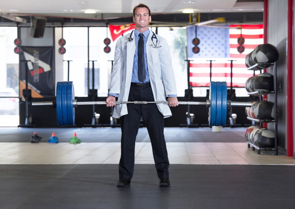 Dr. Schulte — physician and CrossFit athlete, holding a barbell in a white coat